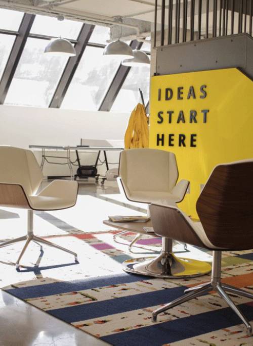 Creative agency lounge space with sign reading 'Ideas Start Here' and colorful modern decor