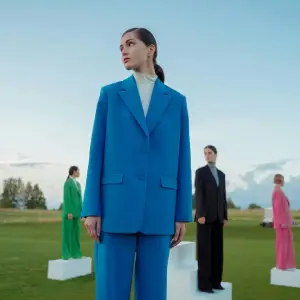 Person in a bright blue suit standing outdoors, with other people spaced across a grassy field